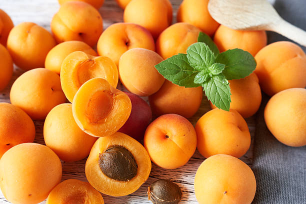 Fresh ripe apricots with mint on wooden table, closeup
